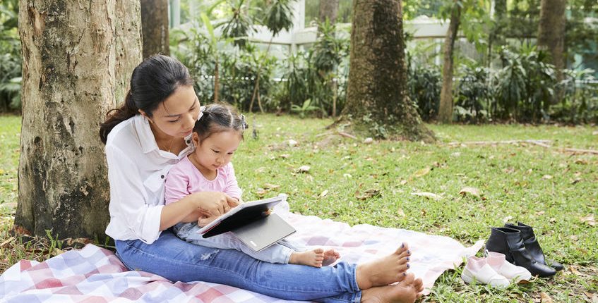 Mother and daughter resting under tree learn and read